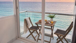 A balcony with a table set for breakfast, a chair, and a potted plant. - Direct Beachfront Paradise: Studio w/ Balcony + Resort Amenities (Cancún)