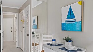 Un couloir avec des portes blanches, un coin repas avec une table et des chaises, et un tableau représentant un voilier accroché au mur.