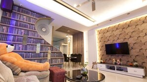 A modern living room with a large bookshelf, a plush sofa, a coffee table, and a flat-screen TV mounted on a hexagonal wall. - Candy House (Wujie)
