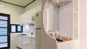 A modern kitchen with white cabinetry, a central island with a sink, and a glass-fronted wine rack. - Candy House (Wujie)