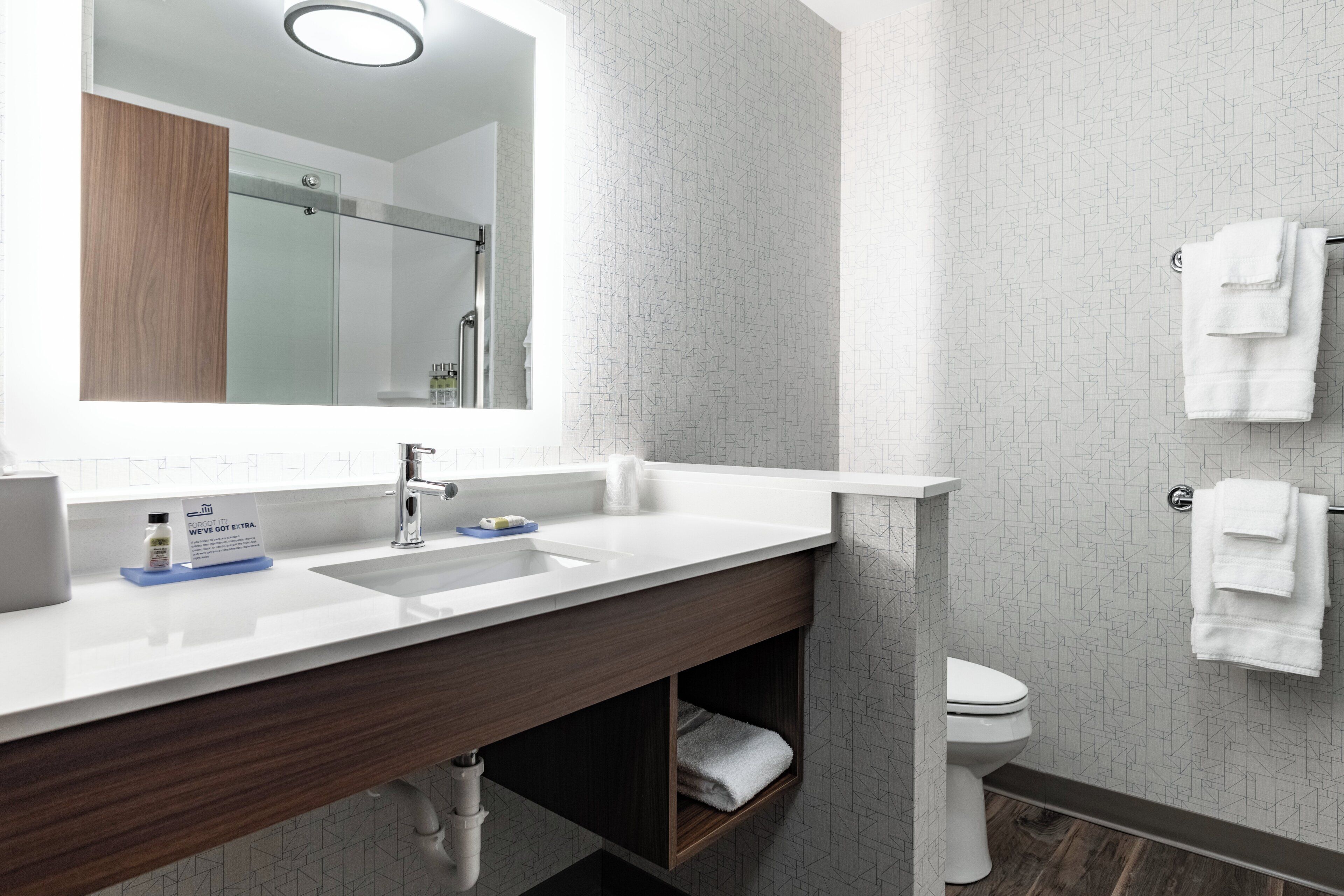 Un baño moderno con un espejo grande, un lavamanos con grifo, un inodoro y un perchero para toallas.