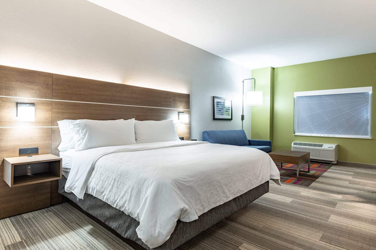 A modern hotel room with a large bed, bedside tables, a desk, a chair, and a large window.