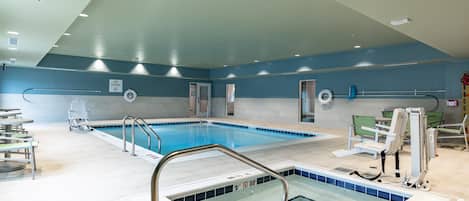 Una piscina interior con un cartel de prohibido bucear, una silla de salvavidas y una escalera de piscina.