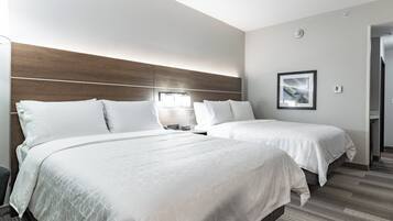 Habitación de hotel con dos camas, cabecera de madera, un cuadro enmarcado en la pared y un termostato visible.