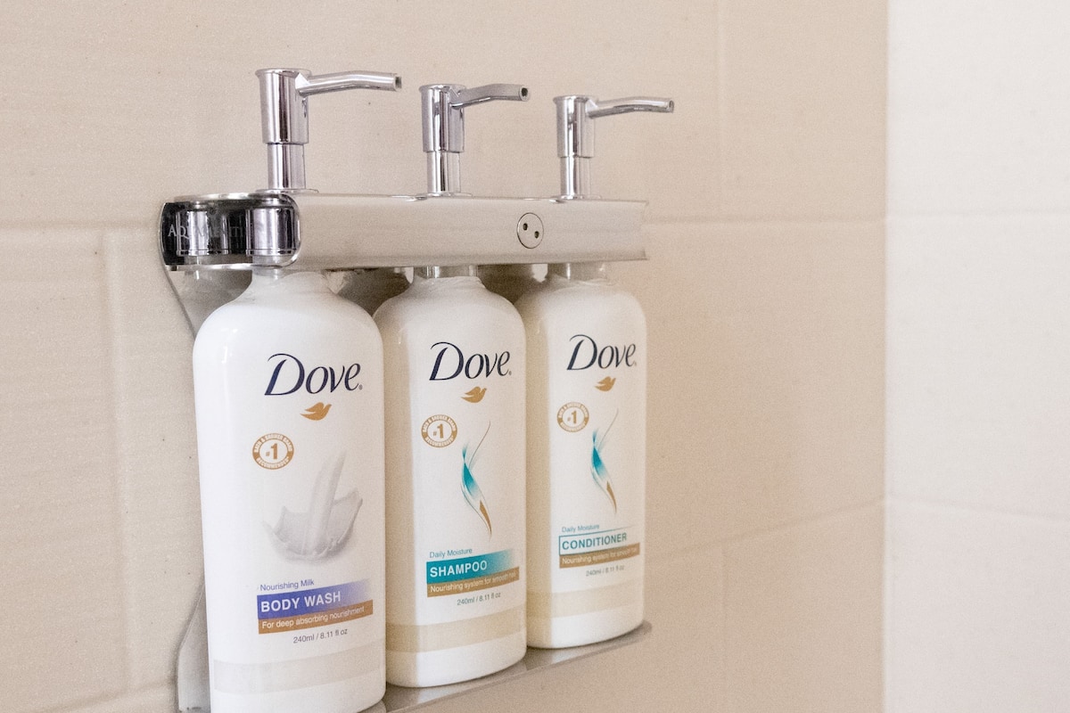 Three Dove body care products mounted on a wall-mounted dispenser.