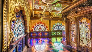An ornate interior with intricate golden designs, stained glass windows, and a checkered floor.