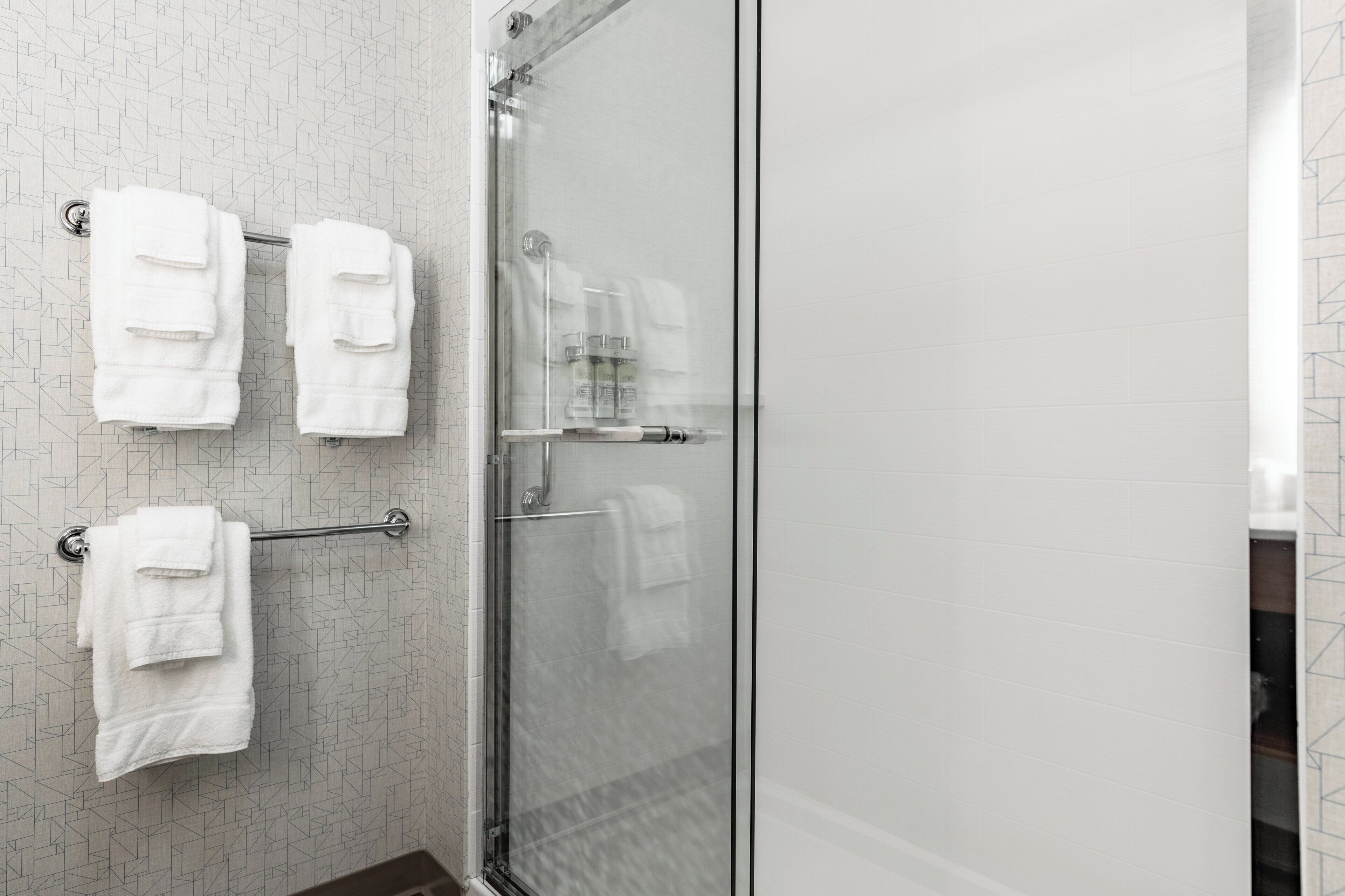 A bathroom with a glass shower enclosure, a towel rack with multiple white towels, and a patterned wall.