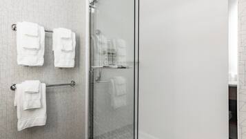 A bathroom with a glass shower enclosure, a towel rack with multiple white towels, and a patterned wall.