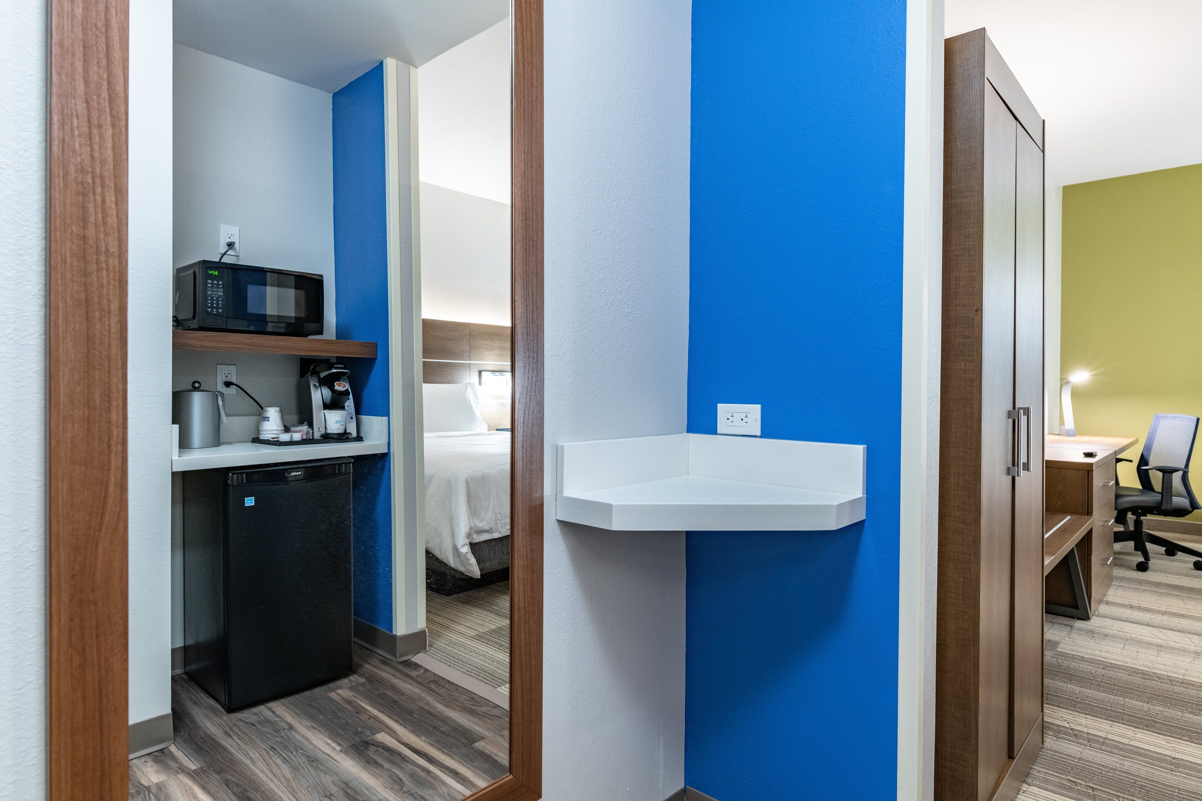 A compact hotel room with a kitchenette, a bed, a desk, and a chair.