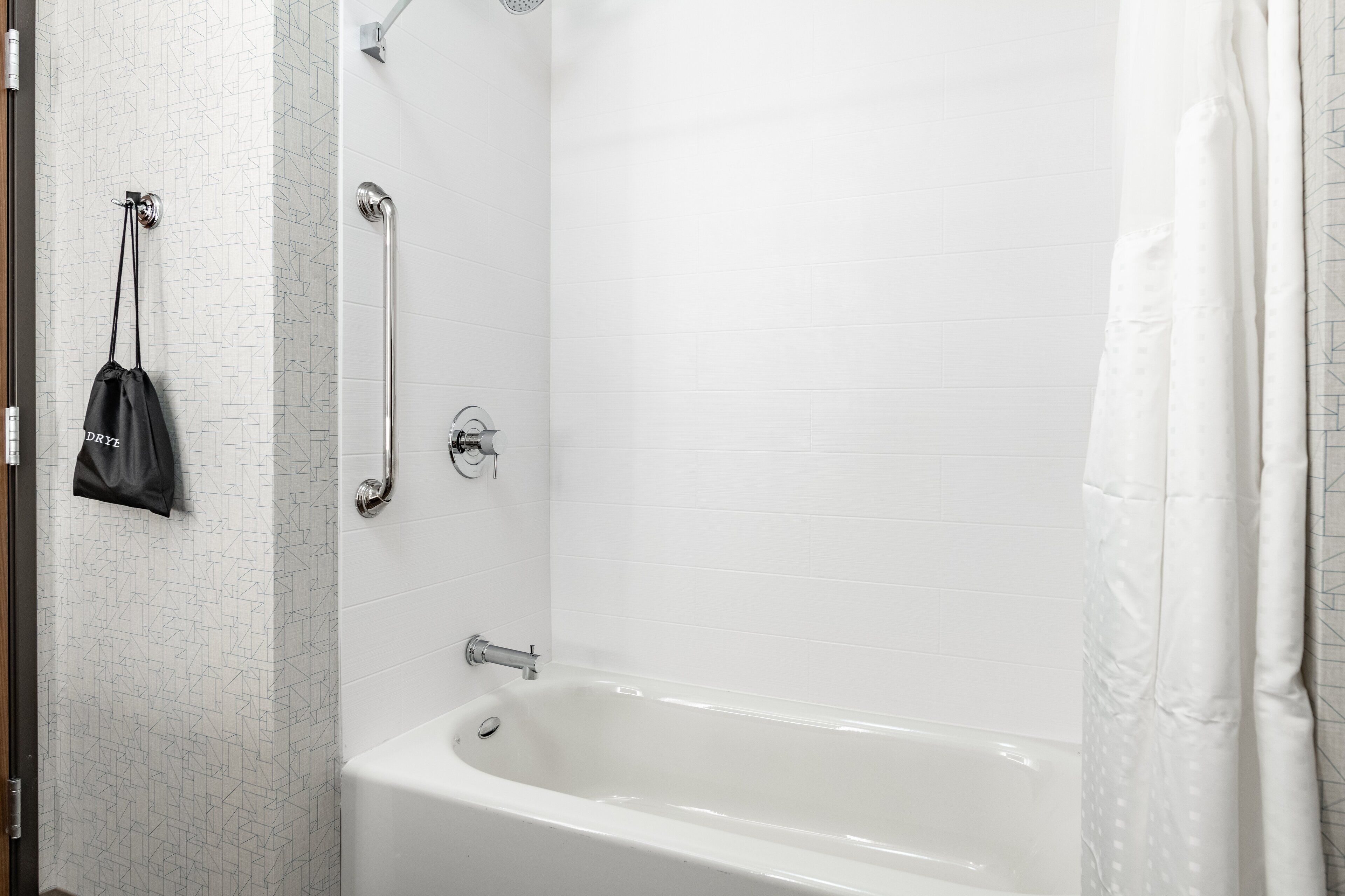 A white bathtub with a shower curtain, a grab bar, and a towel rack with a bag.