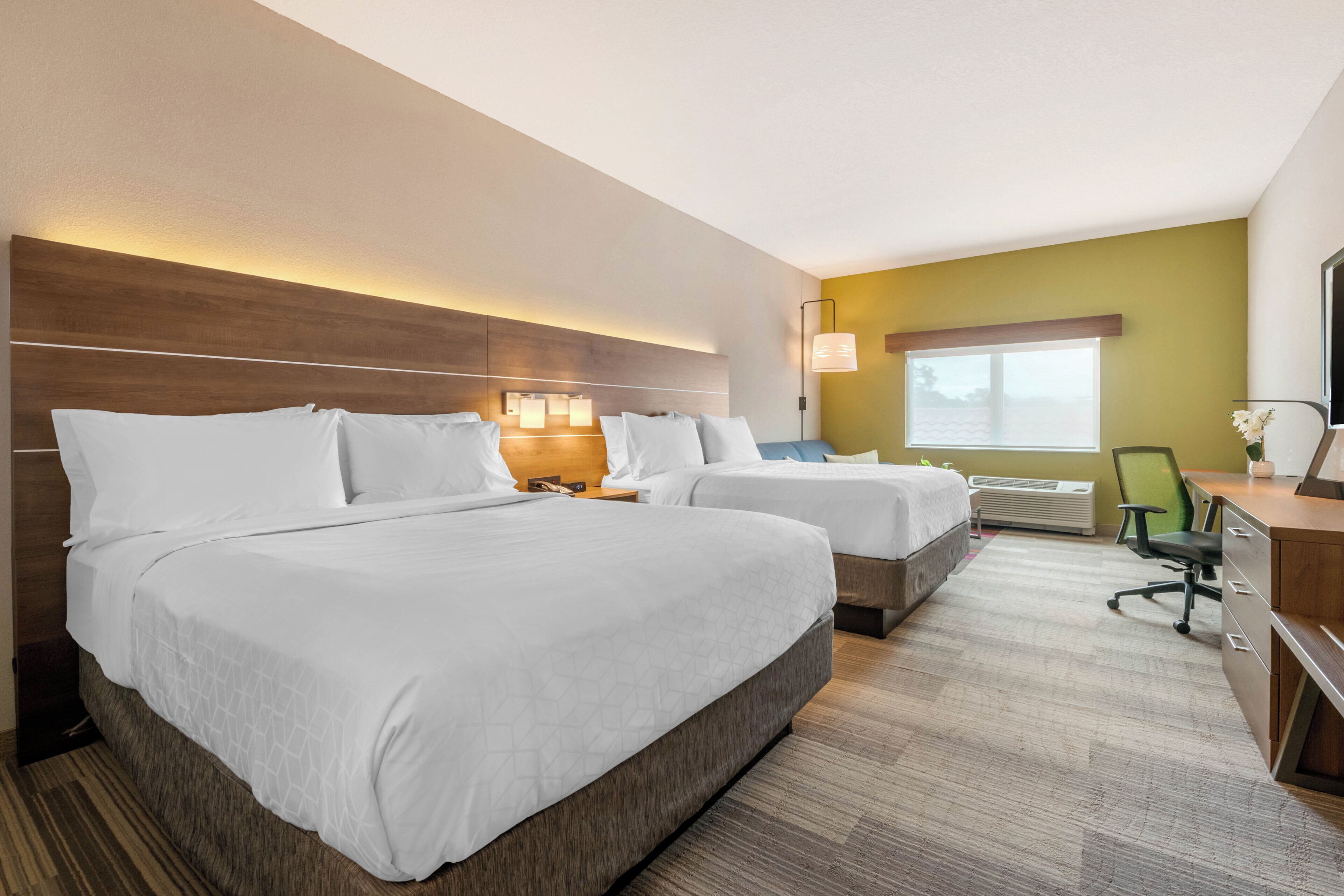 Habitación de hotel con dos camas, un escritorio, una silla y un ventanal.