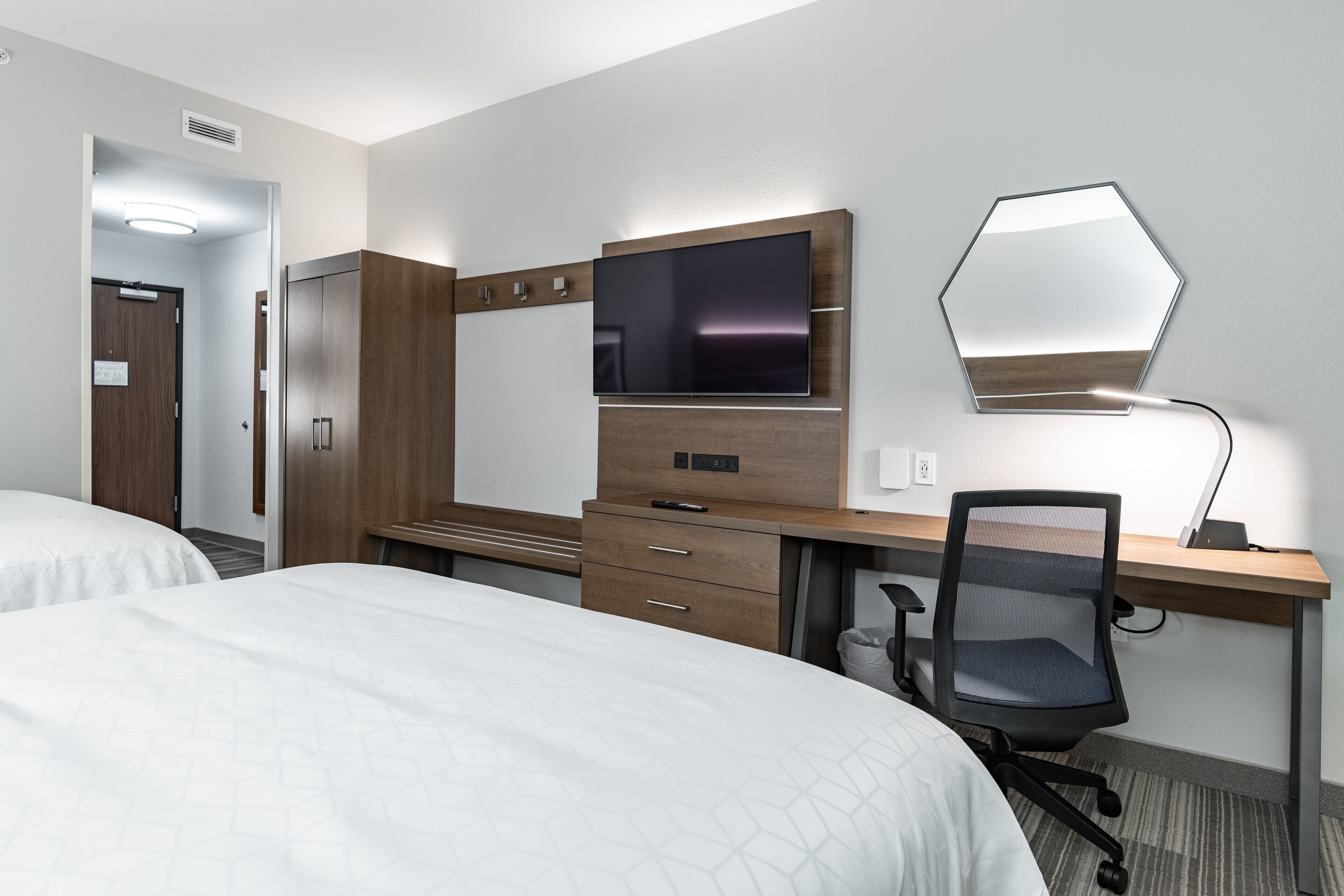 A hotel room with two beds, a desk with a computer, a TV, and a mirror.