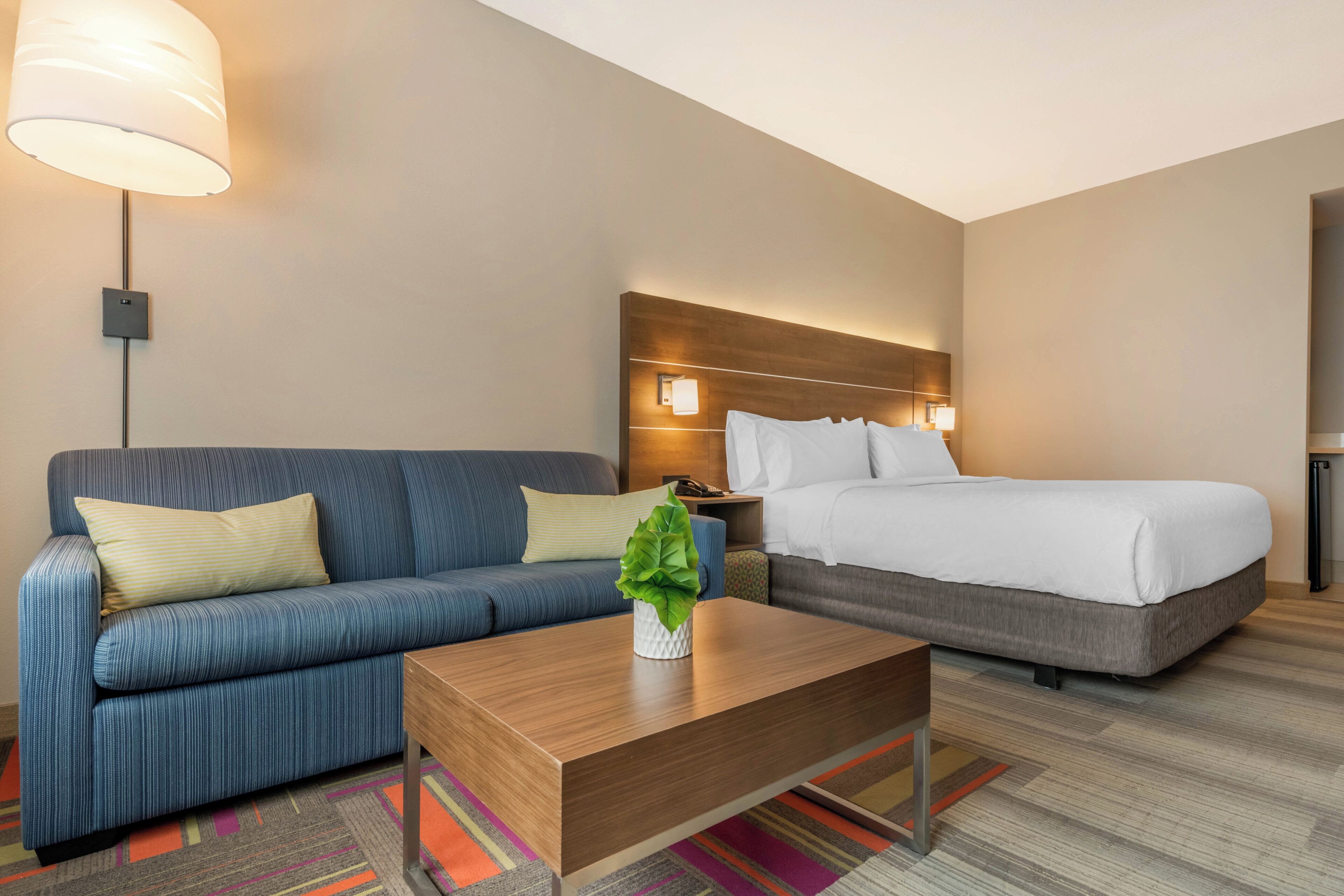 A hotel room with a sofa, a bed, a nightstand, a lamp, and a coffee table.