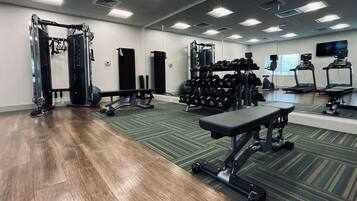 A gym with weightlifting equipment, treadmills, and a mirrored wall.