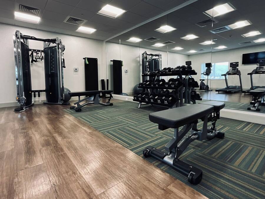 A gym with weightlifting equipment, treadmills, and a mirrored wall.