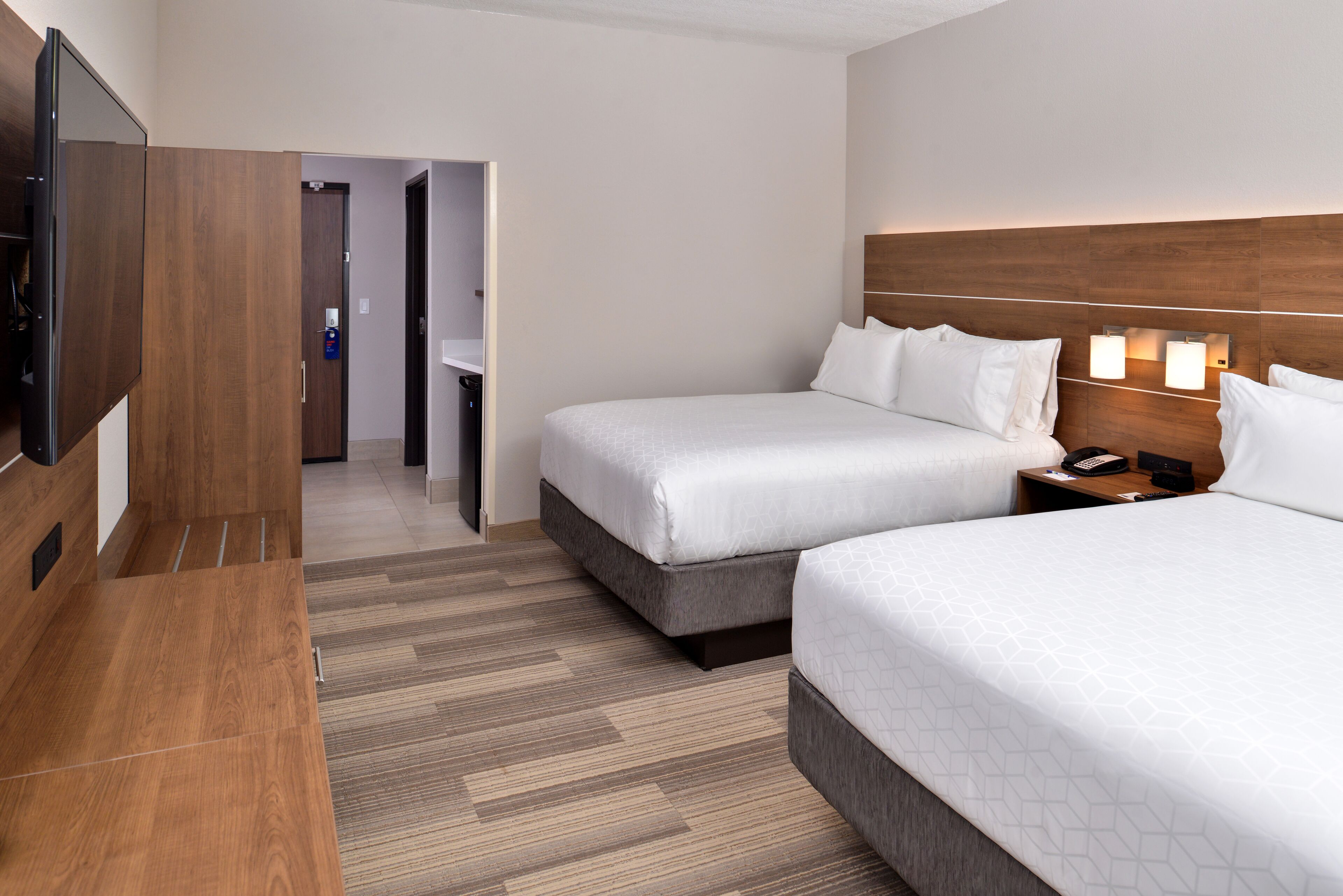 A hotel room with two beds, a TV, a wooden desk, and a nightstand with a phone.