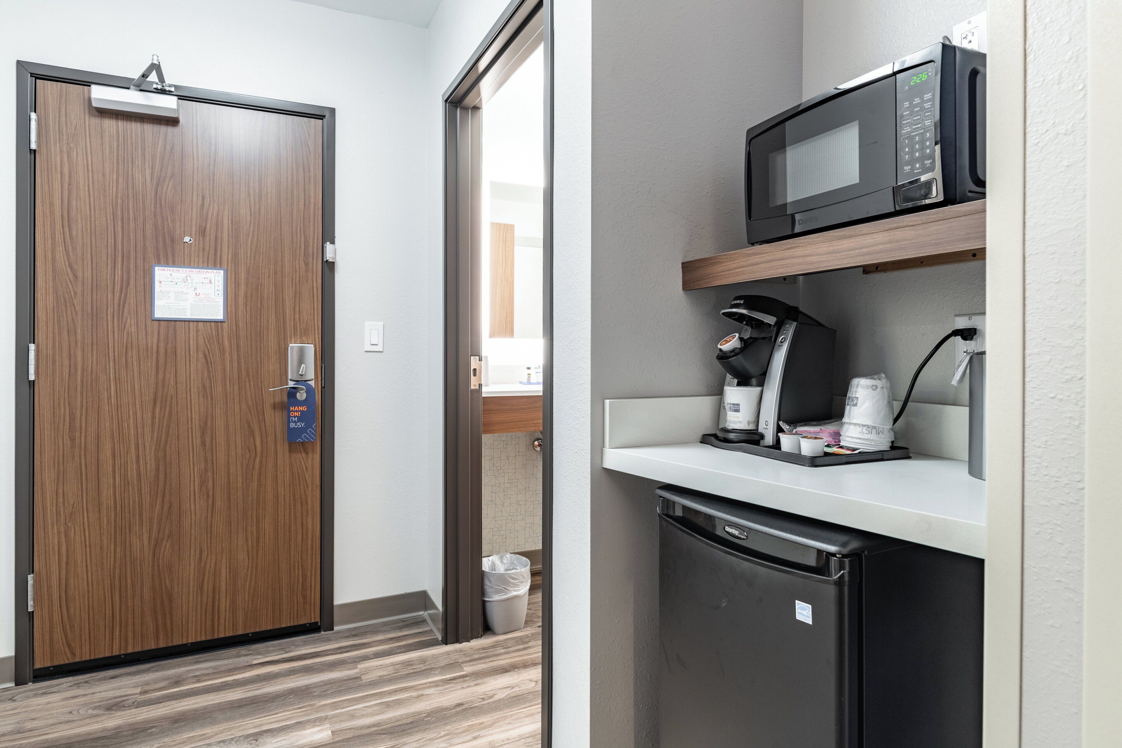 Habitación de hotel con puerta de madera, microondas, cafetera y refrigerador.