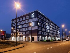 Un hôtel à plusieurs étages au design moderne, caractérisé par une enseigne « NOVOTEL » bien visible, de nombreuses fenêtres par étage et un hall d’entrée bien éclairé.
