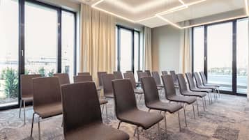 Une salle de conférence avec des rangées de chaises, de grandes fenêtres et un tapis à motifs.
