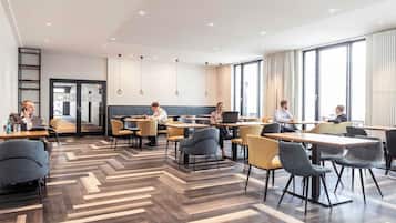 Un espace intérieur moderne, aménagé avec des tables et des chaises, un parquet à motifs en chevrons et un mur en briques.
