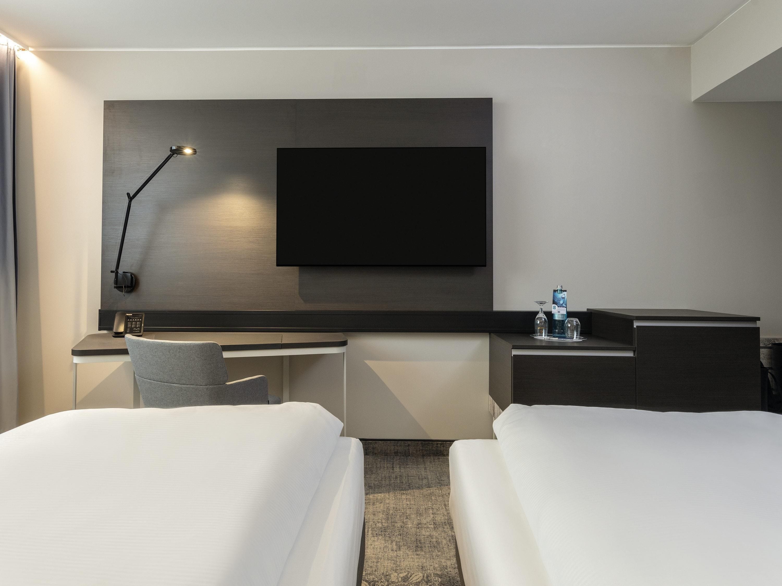 A hotel room with a bed, a desk, a chair, a TV, and a lamp.