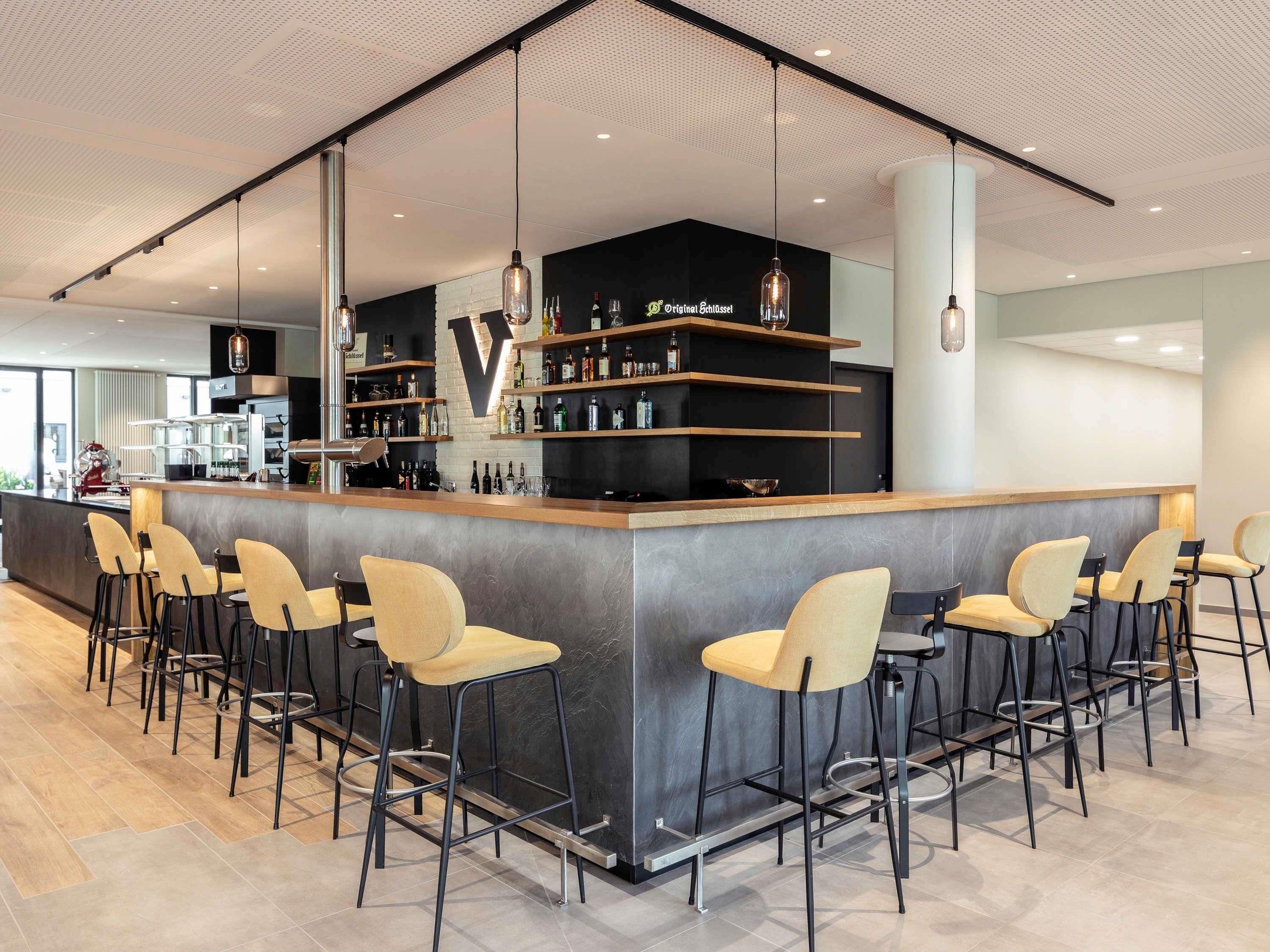 Eine moderne Bar mit hohen Hockstühlen, einer Theke und Regalen voller Flaschen.