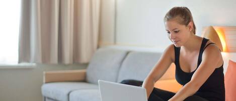 A person sitting on a sofa using a laptop in a room with a window and curtains.