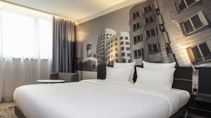 Une chambre d’hôtel avec un grand lit, une petite table ronde et une fresque représentant un paysage urbain sur le mur.