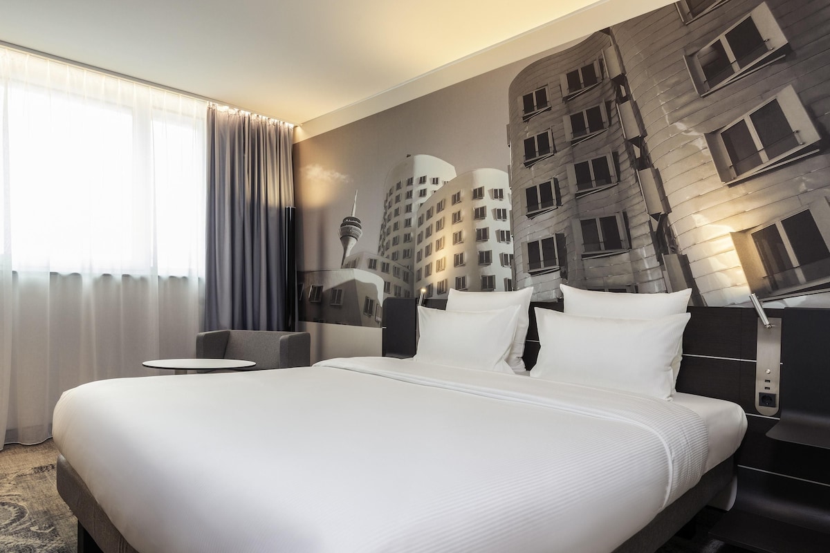 Een hotelkamer met een groot bed, een klein rond tafeltje en een stadsgezicht op de muur.