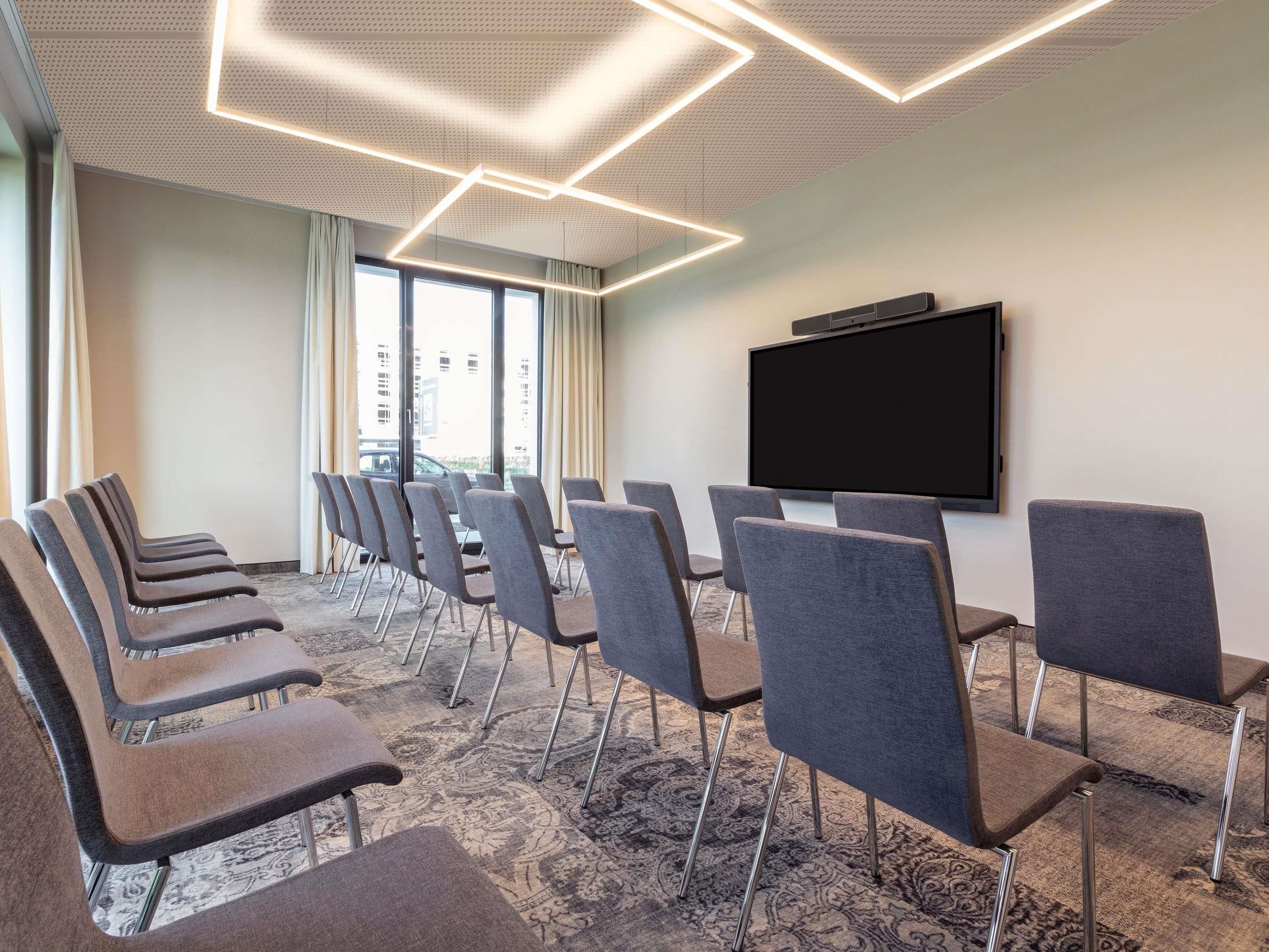 A conference room with rows of chairs, a large screen, and a patterned carpet.