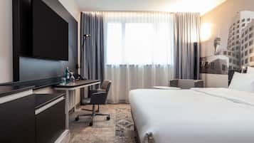 Une chambre d’hôtel comprenant un lit, un bureau avec une chaise, une télévision et une fenêtre avec des rideaux.