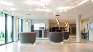Een moderne lobby met grote receptiebalies, een digitaal informatiebord en een stadsgezicht muurschildering.