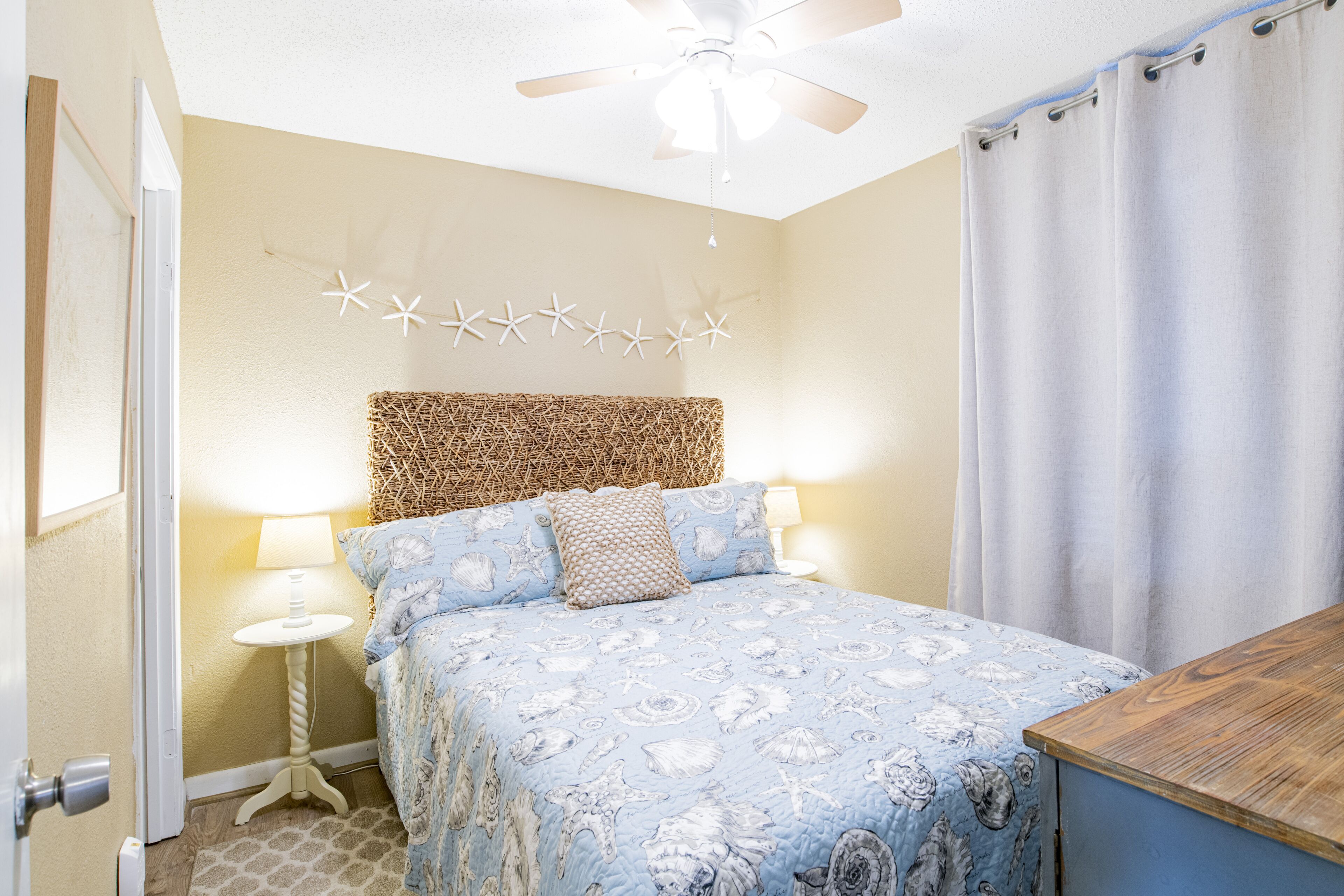 A bedroom with a bed, a ceiling fan, a nightstand, and a wooden dresser.