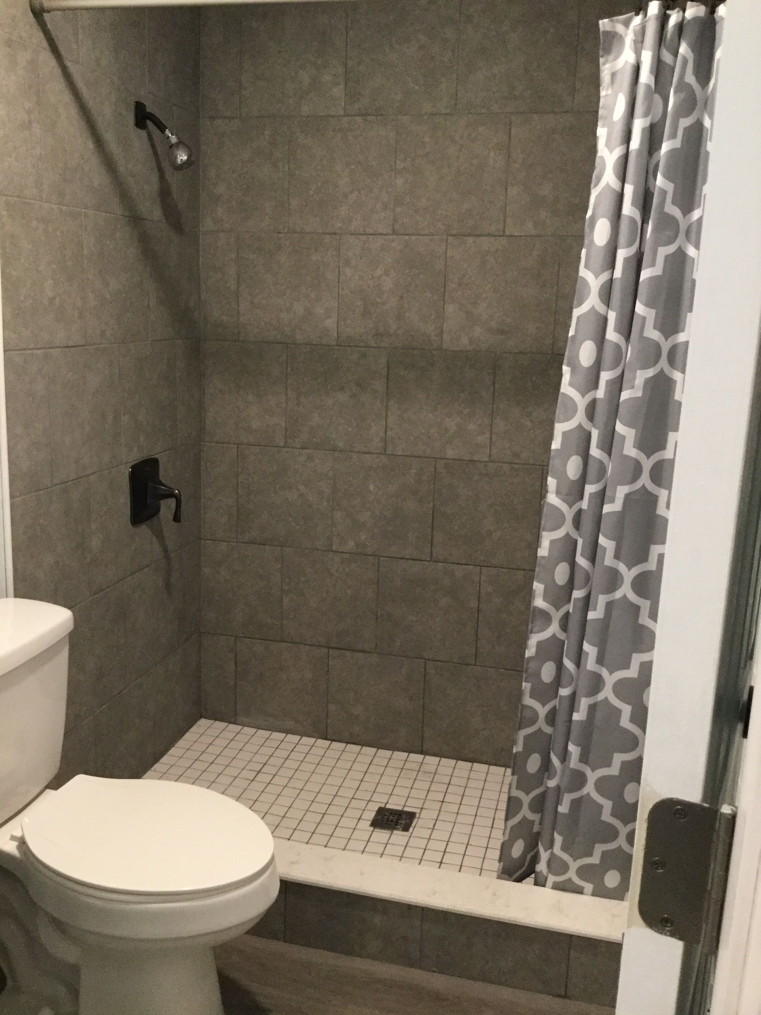 Et badeværelse med brusebad, toilet og flisegulv.