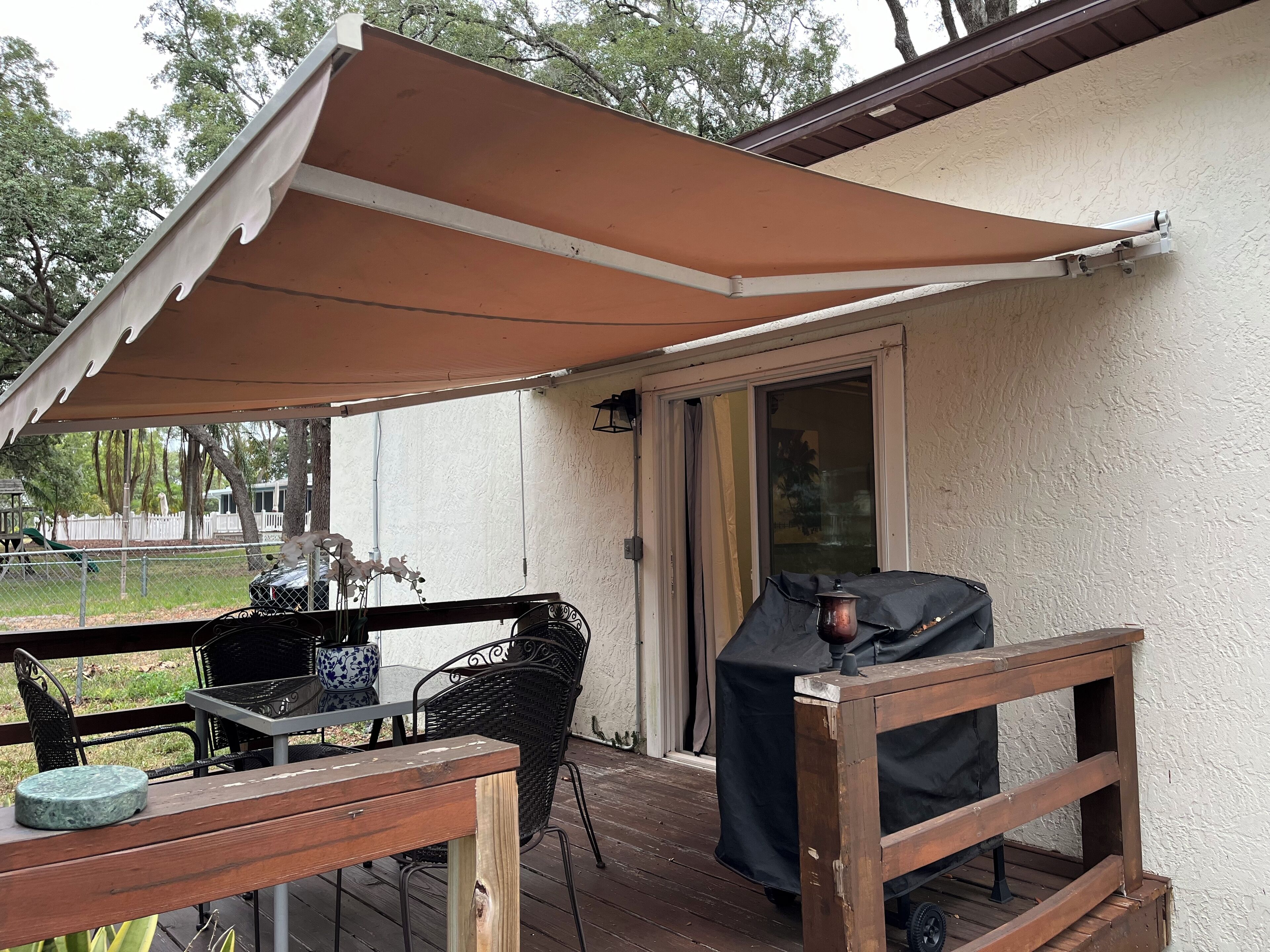 A covered patio with a table and chairs, a grill, and a view of the surrounding area.