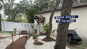 A backyard with a sign reading "Beach House in the Woods," surrounded by trees and a small boat.