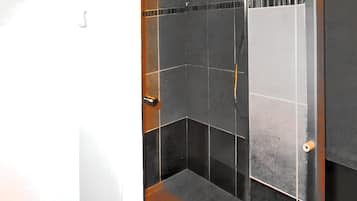 Une salle de bain avec des murs recouverts de carreaux foncés, une zone de douche visible et une poignée de porte.