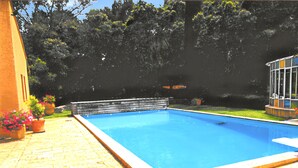 Una piscina rettangolare con un solarium in legno che la circonda, con sullo sfondo alberi e un edificio.