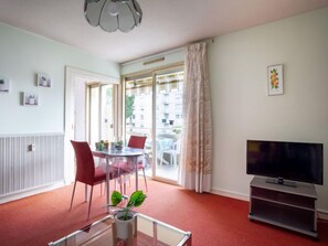 A living room with a dining table, chairs, a TV, and a large window with curtains.