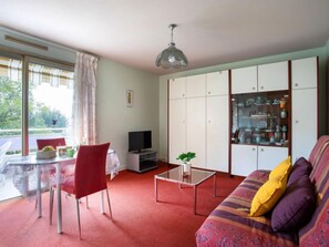 A living room with a sofa, a TV, a glass coffee table, and a dining area with chairs and a table.