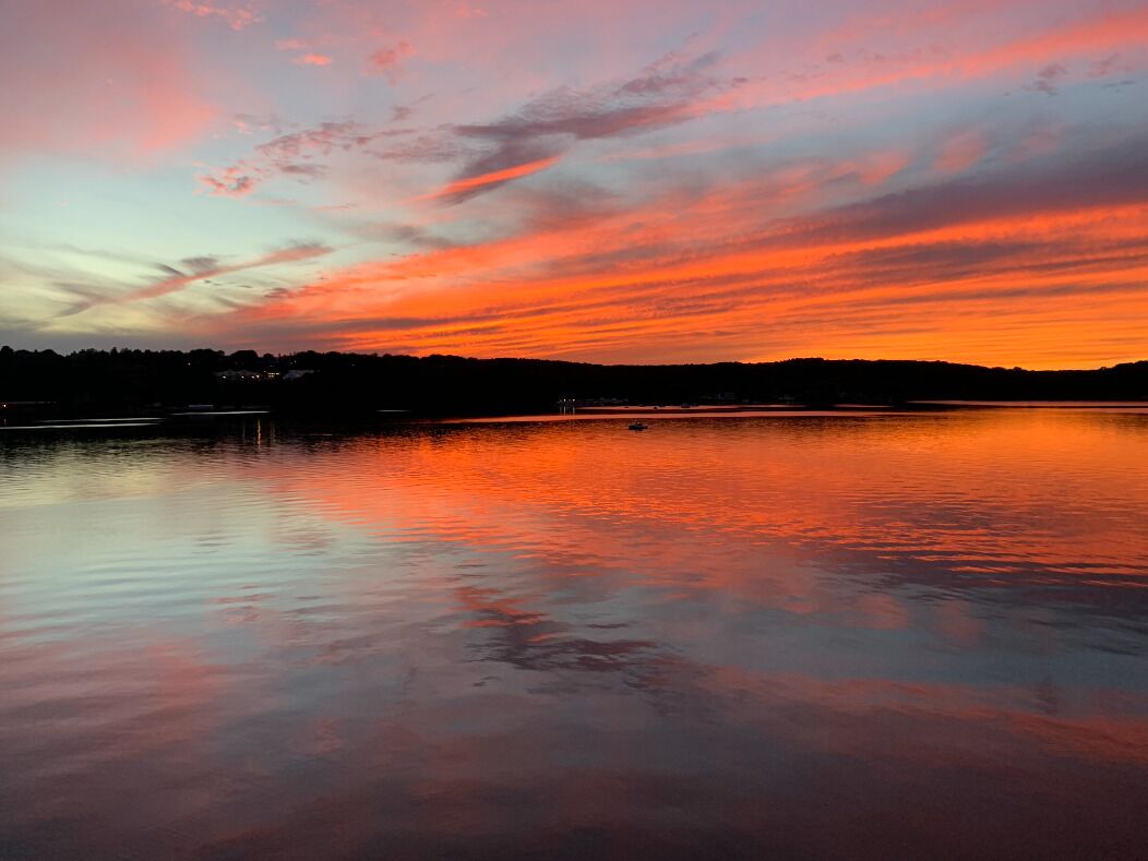 A sunset over a calm lake with a silhouette of a distant shoreline.