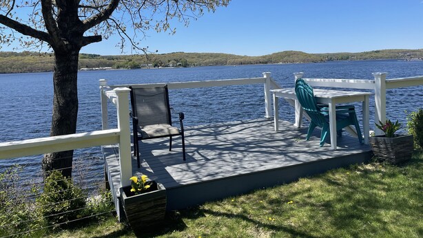 A deck with a table and chairs overlooking a lake, surrounded by a white railing. - Riverfront Home with a View! (Groton)