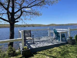 A deck with a table and chairs overlooking a lake, surrounded by a white railing. - Riverside Retreat-Riverfront House  (Groton)
