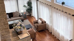 A spacious living room with a stone fireplace, wooden flooring, and large windows offering a view of the water. - Riverfront Home with a View! (Groton)