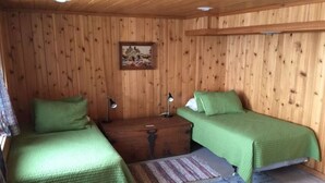 Une chambre rustique en bois avec deux lits, une commode en bois et un tableau accroché au mur.