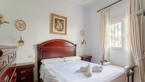 Ein ordentlich eingerichtetes Schlafzimmer mit einem großen Bett, einem Schminktisch, einem Nachttisch und einem Fenster mit Vorhängen.