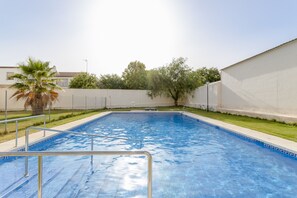 A swimming pool with a metal ladder, surrounded by a white wall and a grassy area with trees.