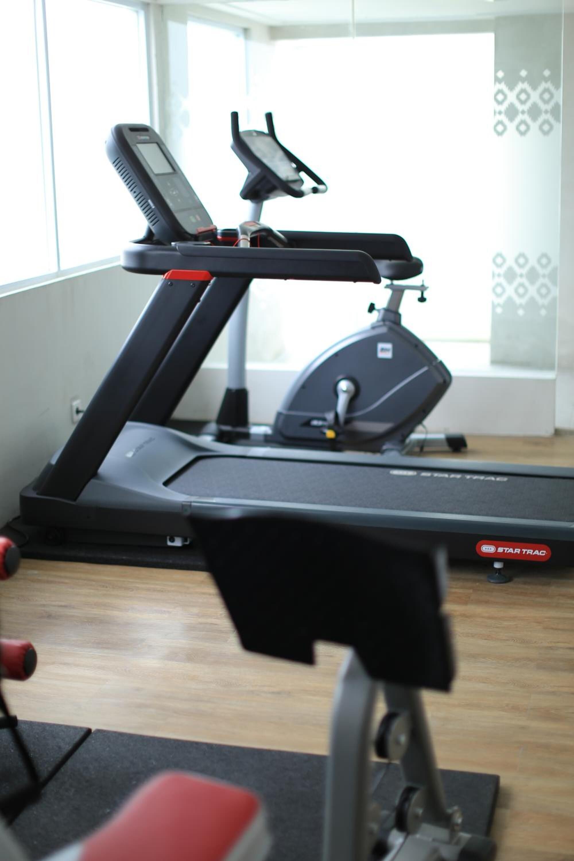 Una cinta de correr en una habitación con ventanas amplias y un papel tapiz decorado.