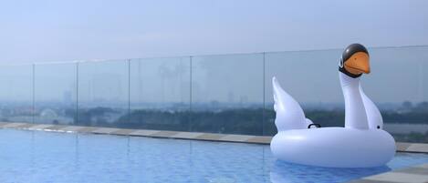 A swan-shaped inflatable in a clear pool with a cityscape view.