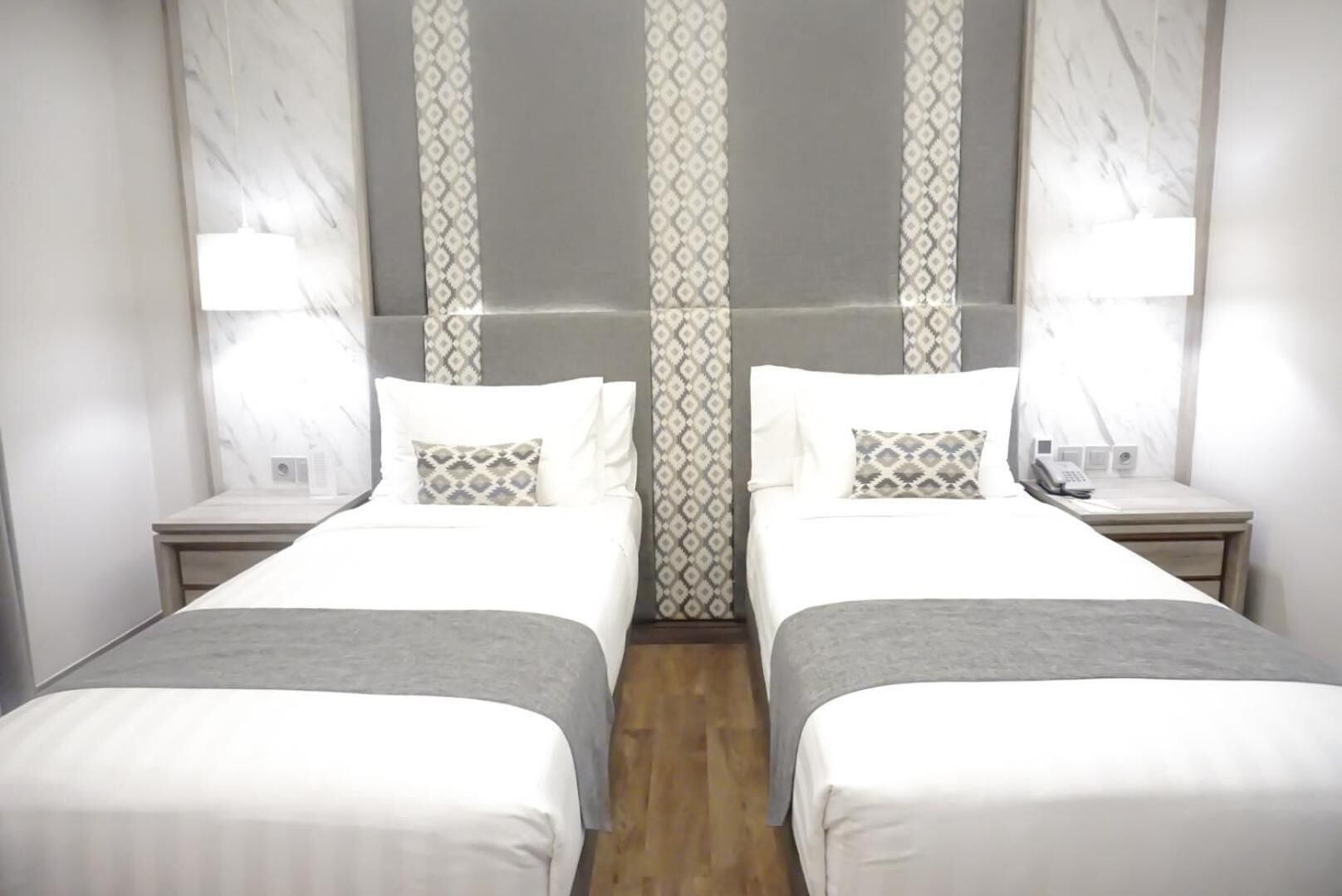 Una habitación de hotel con dos camas, suelo de madera, cortinas estampadas y lámparas de noche.